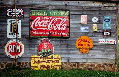 Collection of vintage advertising signs on rustic wooden wall showcasing classic brands.